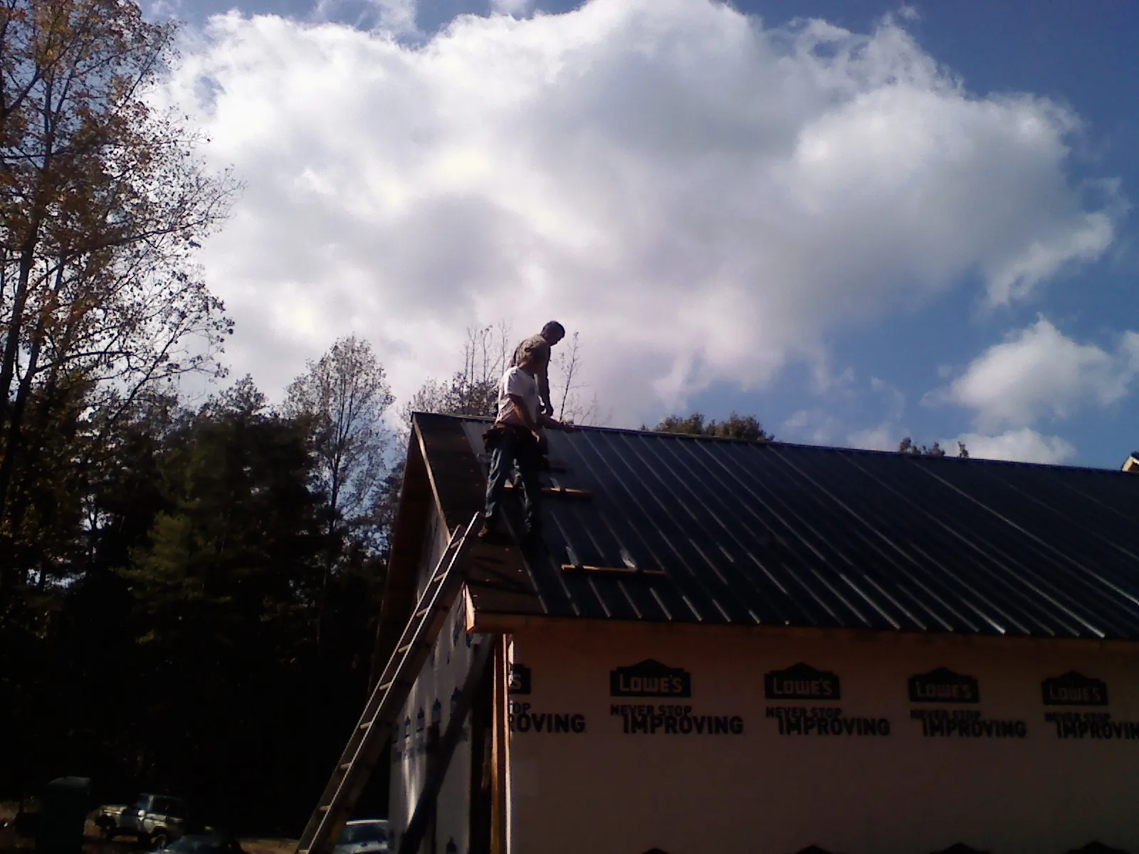 Roofer fastening dark metal panels high against a cloudy sky, from a Roof Inspection job in Hills